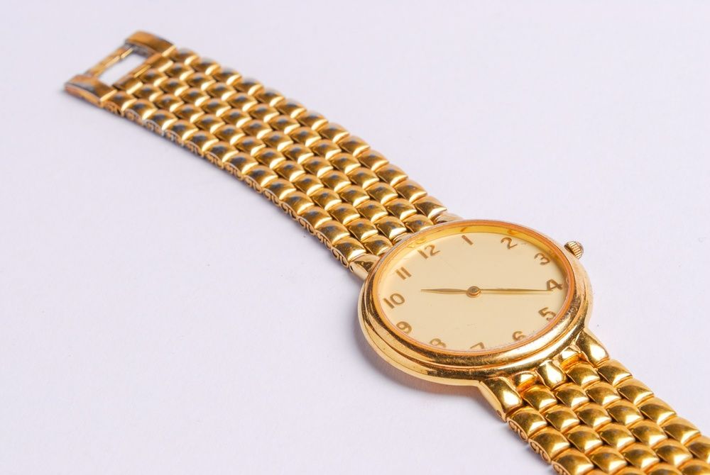 Reloj de pulsera dorado con esfera redonda y brazalete de eslabones sobre fondo blanco.