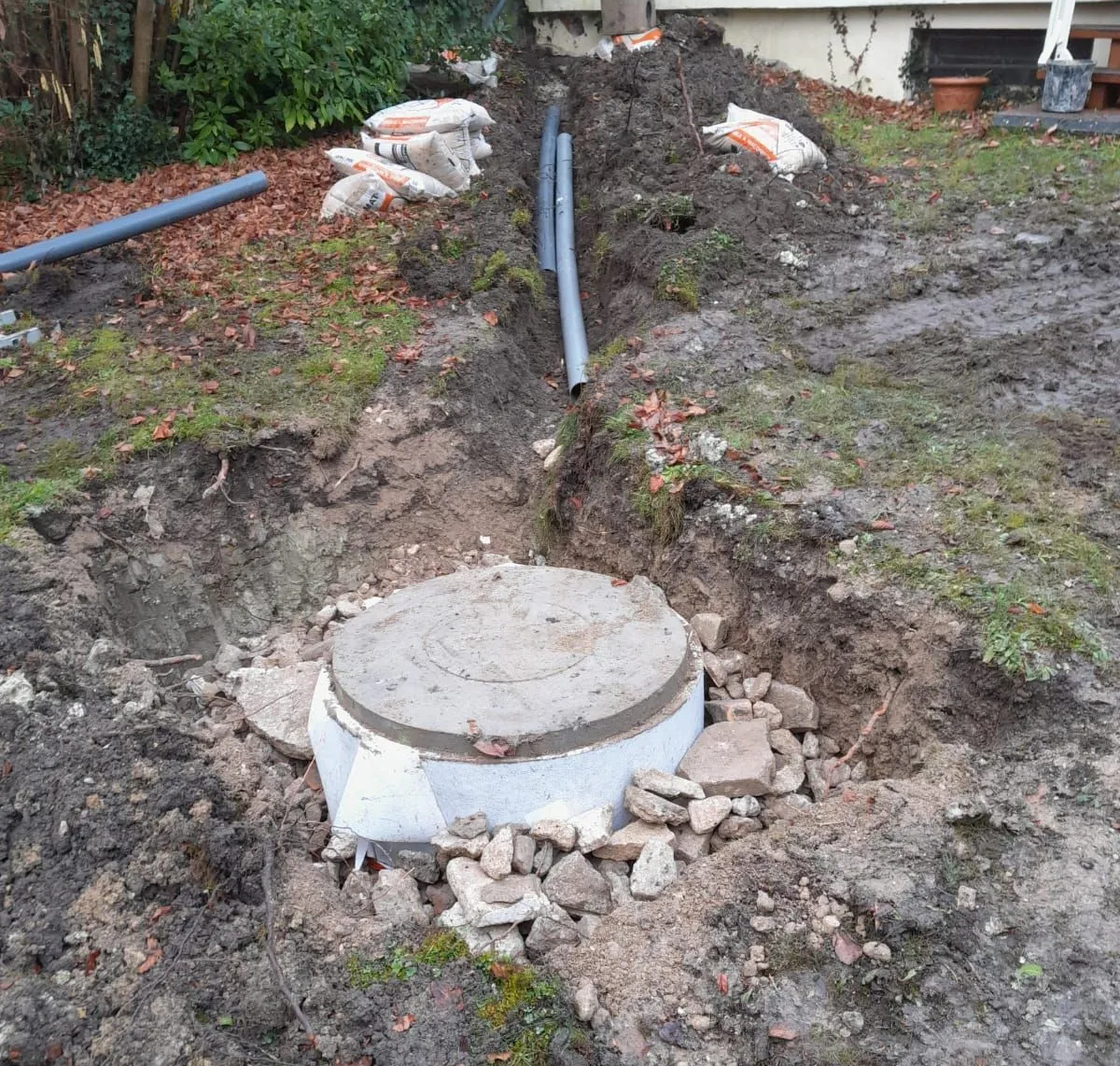 Un système de drainage en béton en construction dans un sol boueux, avec un couvercle de regard et des canalisations.