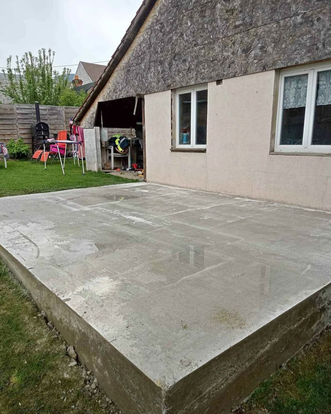 Terrasse en béton fraîchement coulée à côté d'une maison avec pelouse.