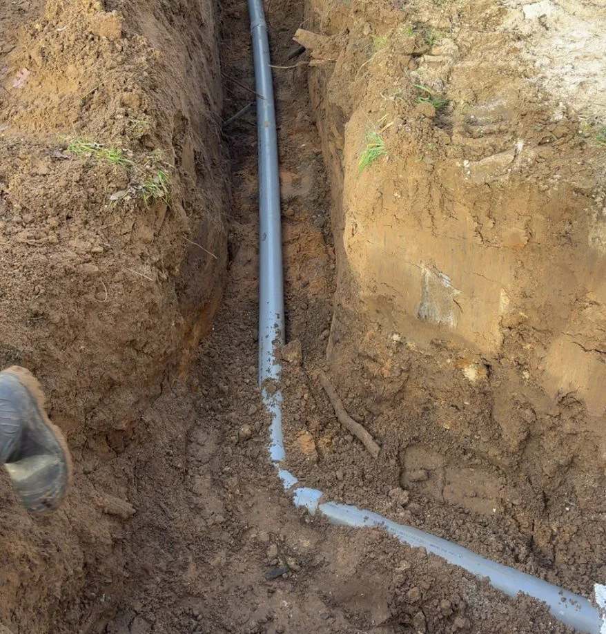Une tranchée traversée par un tuyau gris, probablement pour la plomberie ou les services publics.