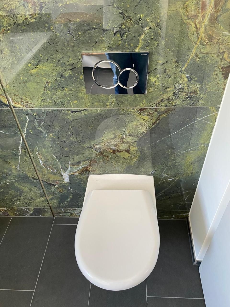 Eine Toilette in einem Badezimmer mit einer grünen Marmorwand dahinter. Foto von der MS Sanitär Heizung GmbH