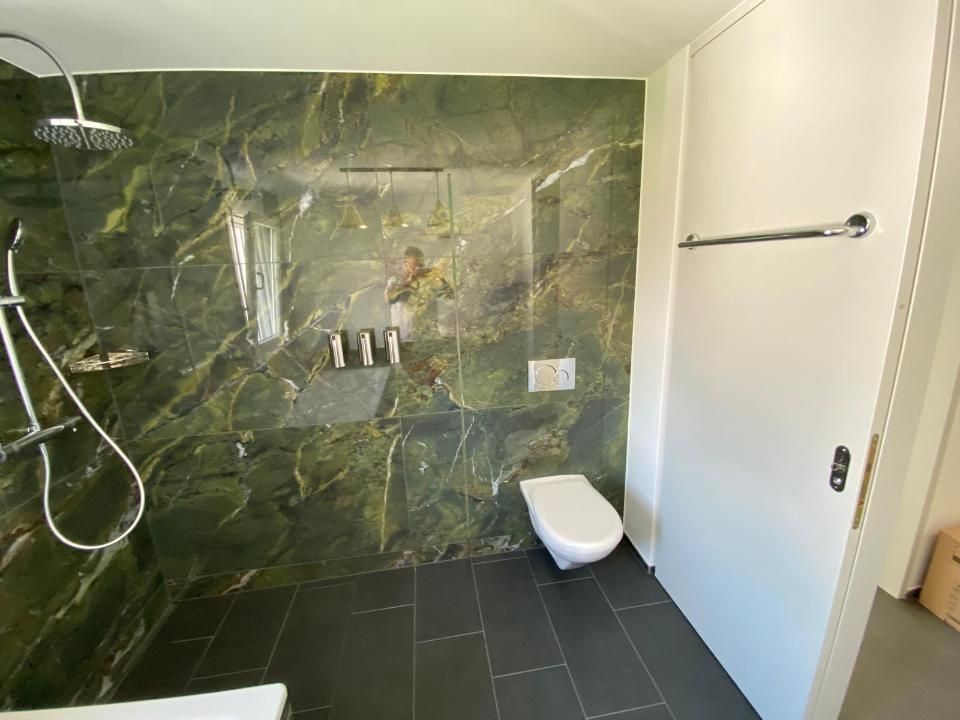 Ein Badezimmer mit Toilette, Dusche und Wänden aus grünem Marmor. Foto von der MS Sanitär Heizung GmbH