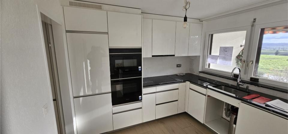 Eine Küche mit weissen Schränken und schwarzen Arbeitsplatten und einem Fenster. Foto von der MS Sanitär Heizung GmbH