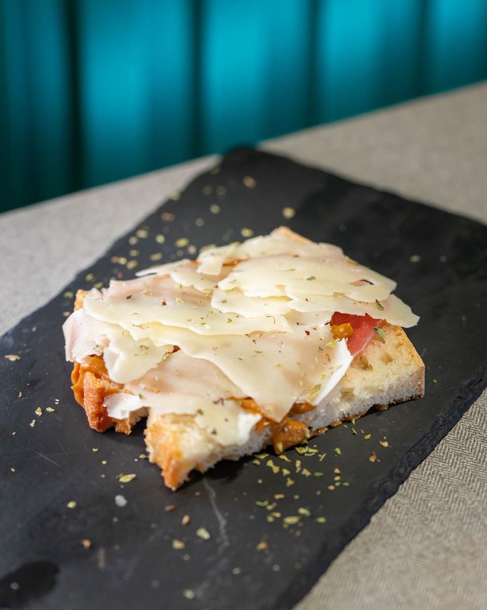 Un trozo de focaccia cubierto con parmesano rallado y hierbas, servido sobre una losa de piedra negra.
