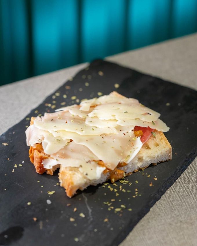Un trozo de focaccia cubierto con parmesano rallado y hierbas, servido sobre una losa de piedra negra.