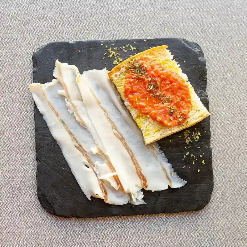 Una rebanada de pan tostado con tomate, un vaso de zumo de naranja y una taza de café humeante sobre una mesa de madera.