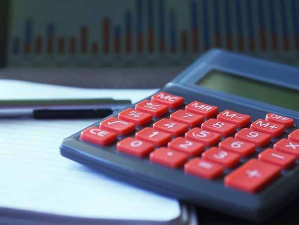 Una calculadora negra con botones rojos se encuentra sobre una mesa junto a un bolígrafo.