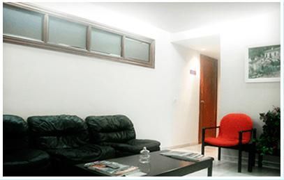 Sala de estar luminosa con sofá oscuro, mesa de centro de cristal, silla roja y puerta abierta.