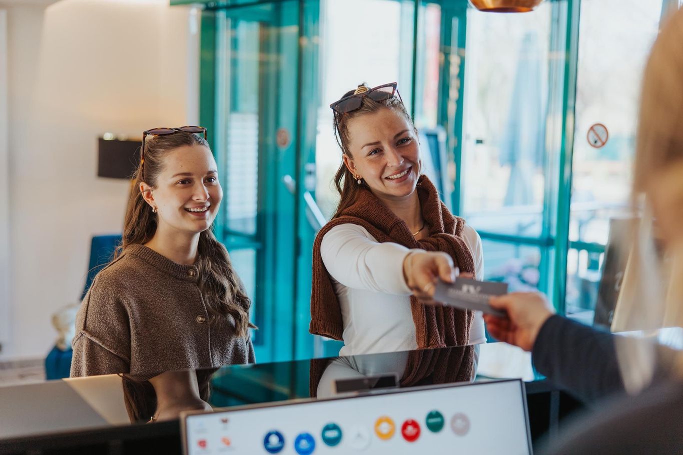 Zwei lächelnde Kollegen tauschen an einem Empfangstresen in einer hellen Bürolobby eine Visitenkarte aus.