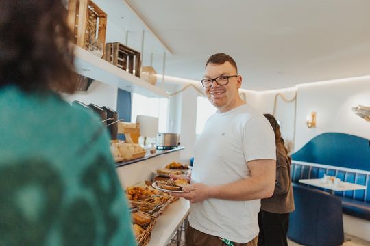 Frühstücksteller aus einem Café mit Brötchen, Gebäck, Obst und einem Latte auf einem Tisch