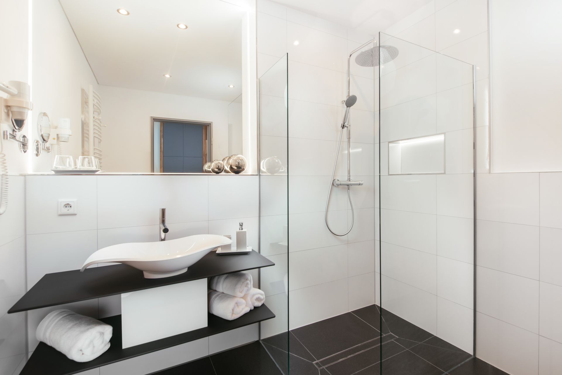 Ein Badezimmer mit ebenerdiger Dusche, Waschbecken und Spiegel.