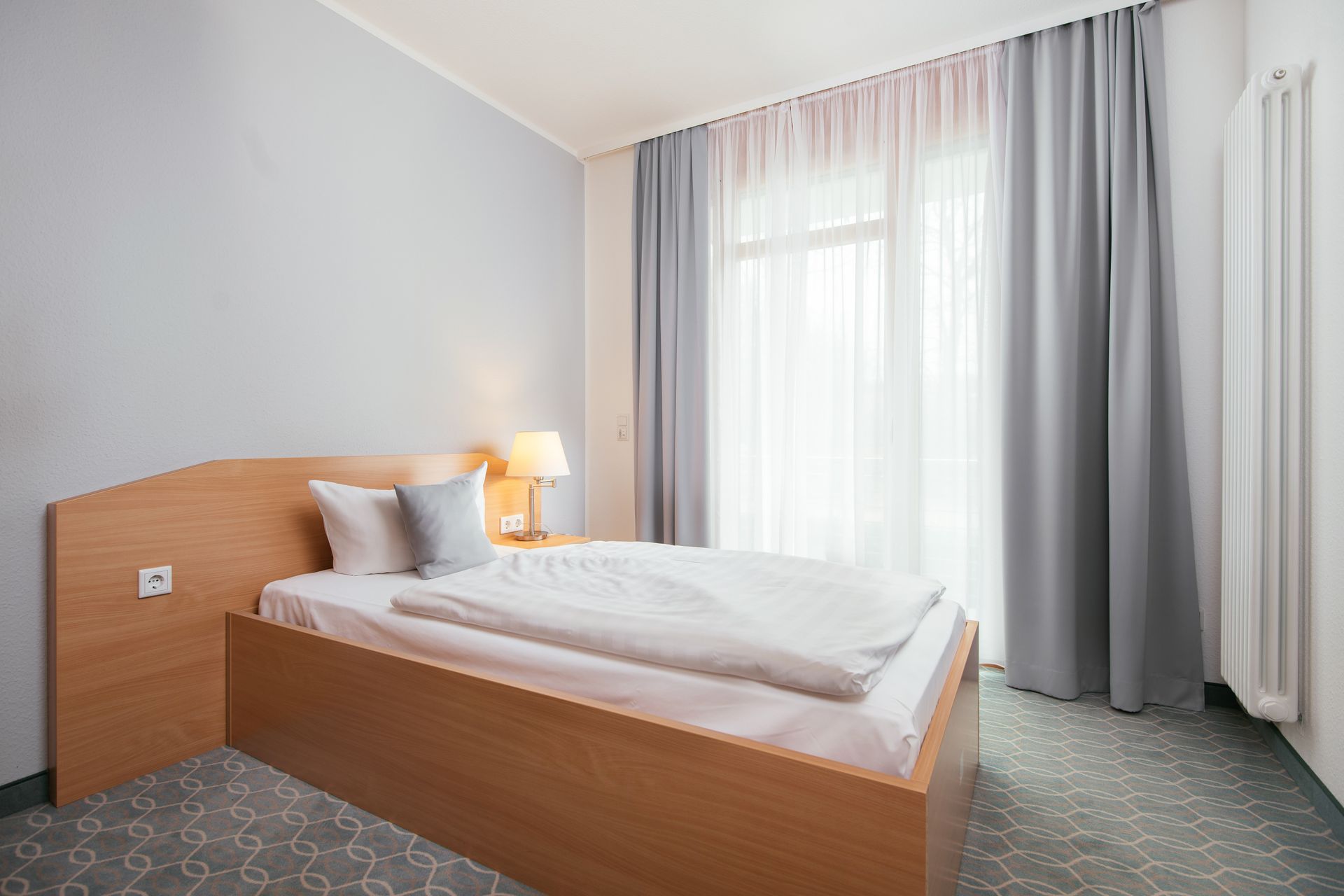 Ein Hotelzimmer mit Bett, Fenster und Vorhängen.