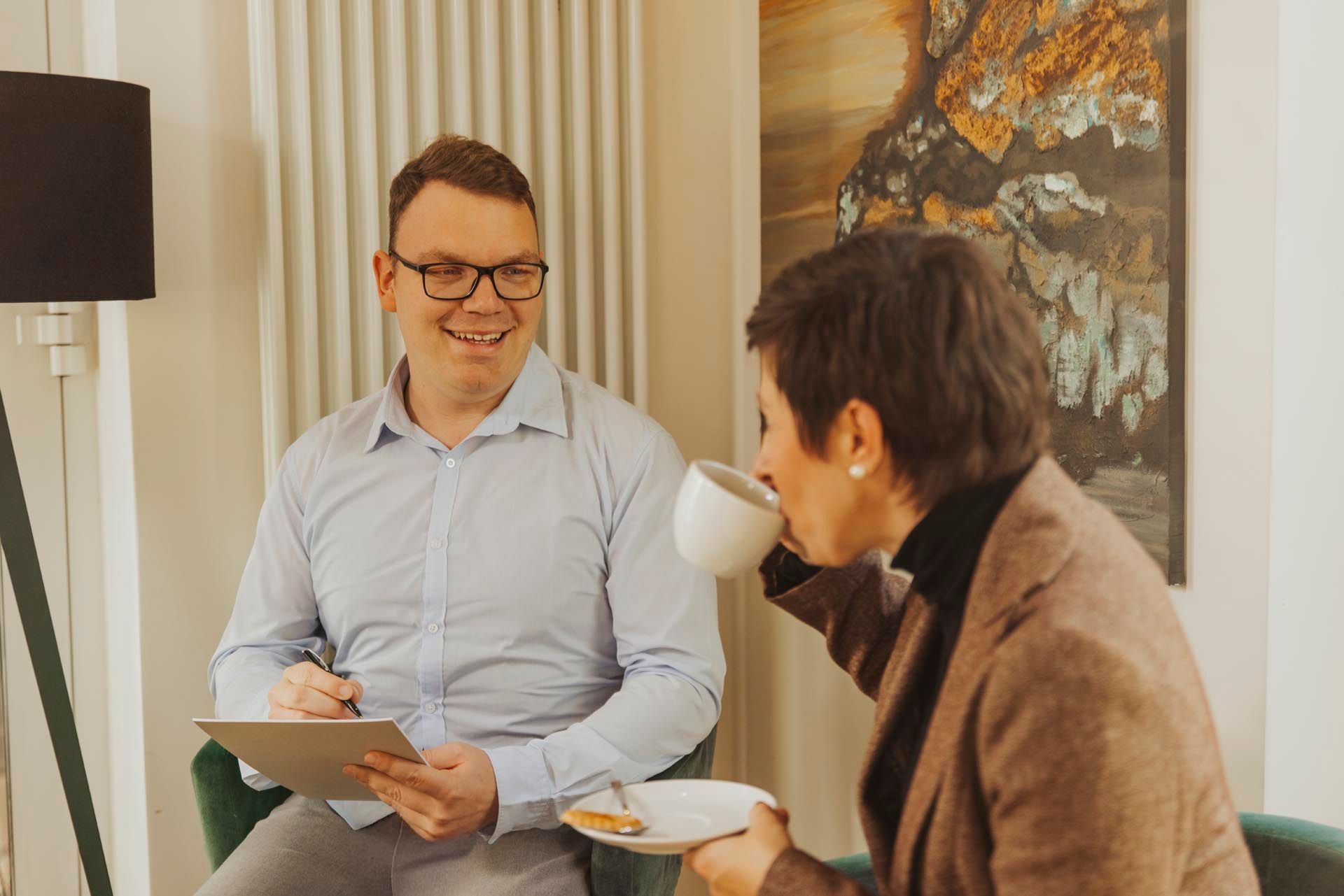 Ein Mann und eine Frau sitzen auf einem Sofa, trinken Kaffee und unterhalten sich.