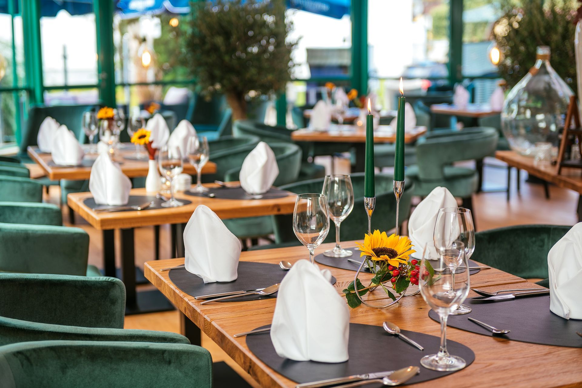 Restaurant-Speisesaal mit gedeckten Tischen; smaragdgrüne Stühle, Holztische, weiße Servietten und Kerzen.