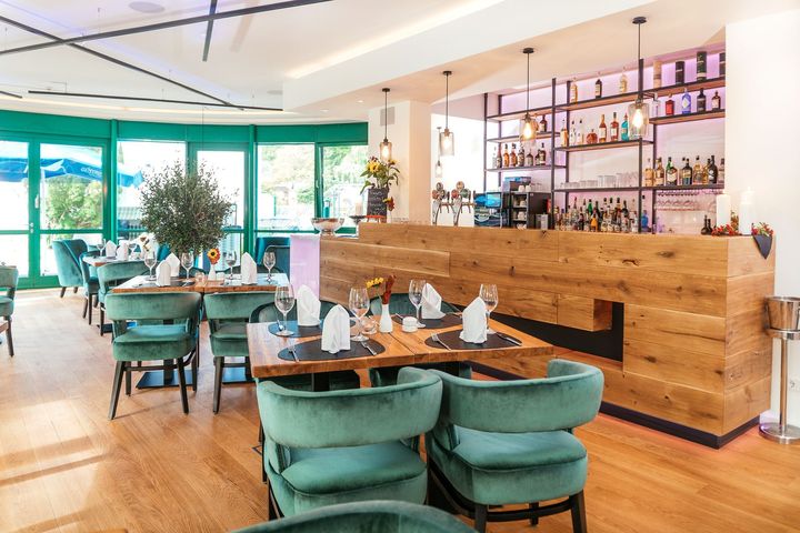 Helles, modernes Restaurantinterieur mit türkisfarbenen Stühlen, Holzbar und großen Fenstern