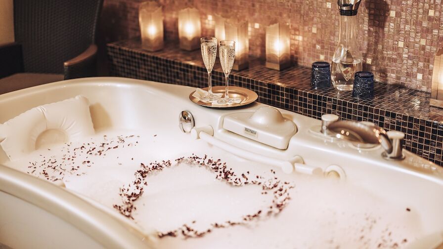 Eine mit Schaum gefüllte Badewanne und Kerzen in einem Badezimmer.