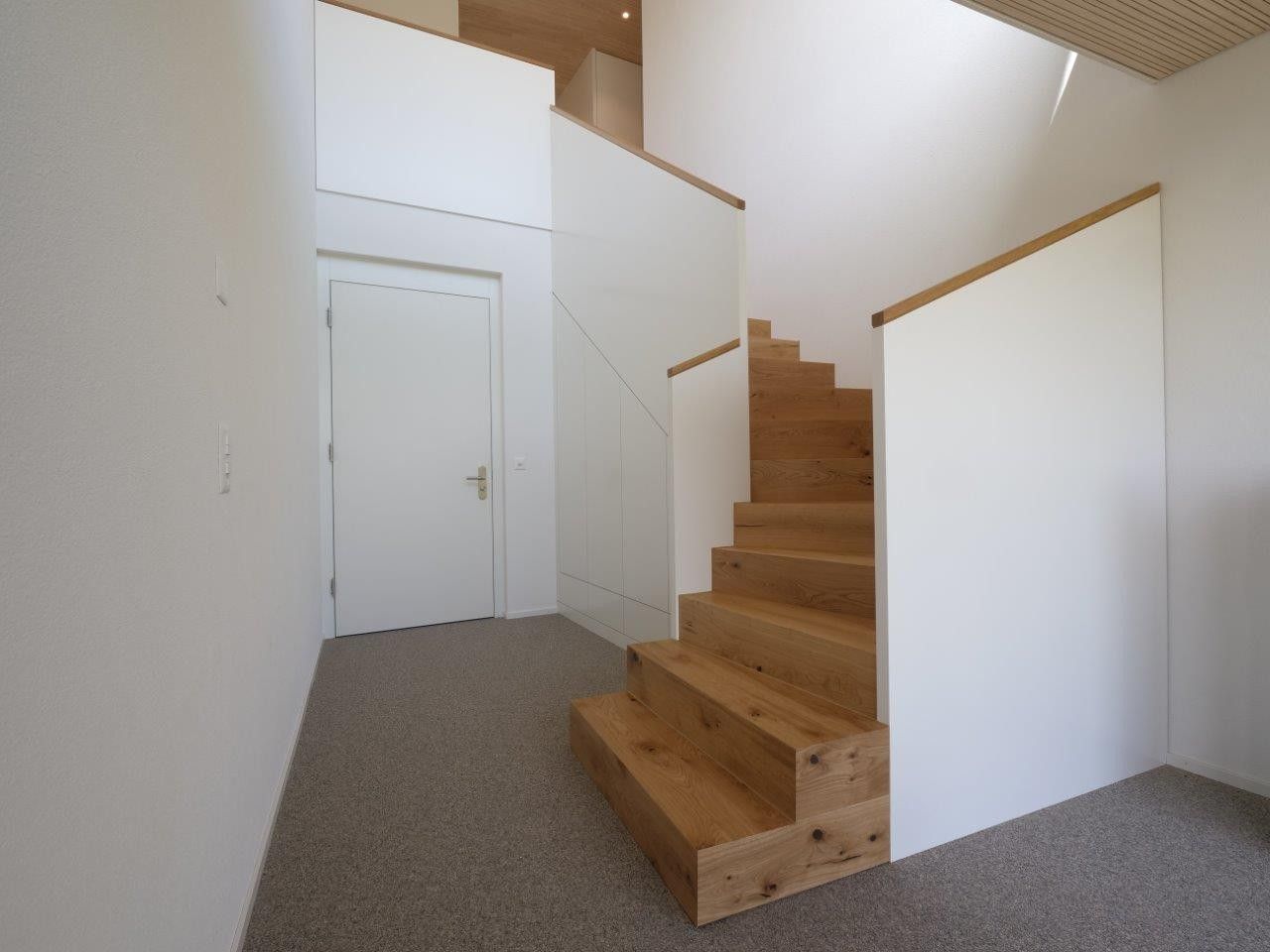 Weiße Schränke unter einem Fenster, obenauf ein Regal, davor eine Pflanze.