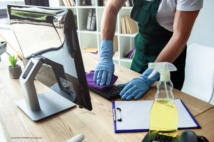 Multiline GmbH - Mann mit Gummihandschuhen reinigt sorgfältig die Tastatur an einem Schreibtisch