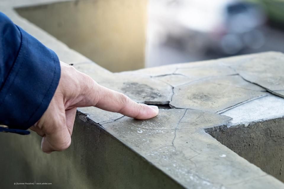 Multiline GmbH - Hand mit ausgestrecktem Finger auf einer Betonmauer mit Rissen und Löchern