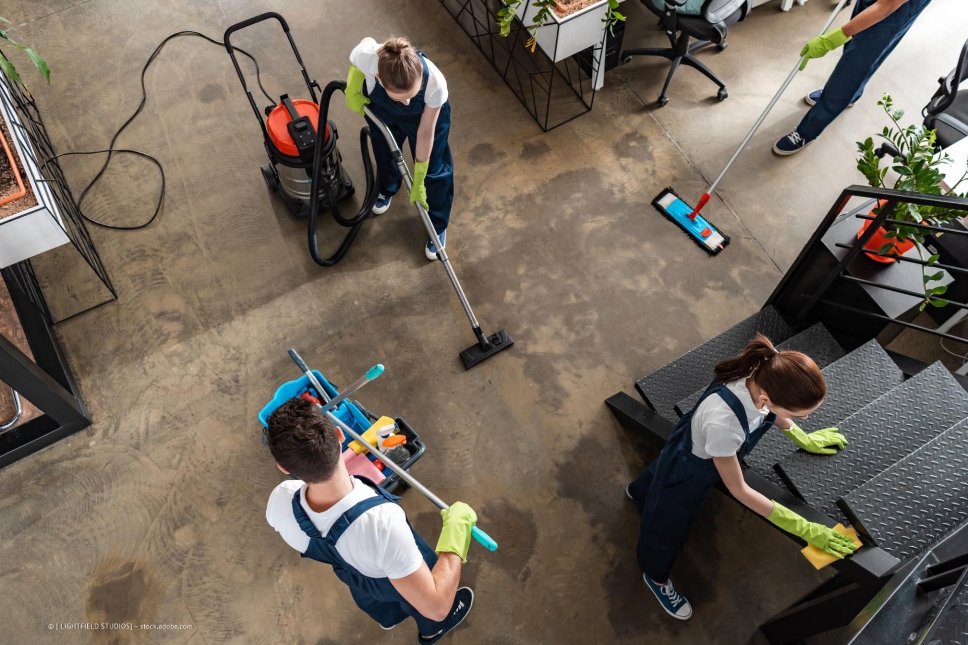 Multiline GmbH - Vier Reinigungsfachkräfte mit Staubsauger, Wischmopp und Schwamm reinigen Fußboden und Treppe eines rustikalen Innenbereichs.
