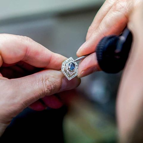 Des mains tiennent une bague en diamant ornée d'une pierre précieuse bleue, probablement en cours de fabrication.