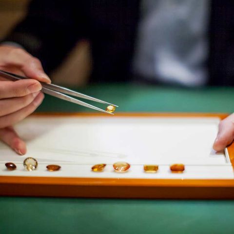 Une personne utilise une pince à épiler pour examiner une pierre précieuse parmi d'autres gemmes présentées sur un plateau.