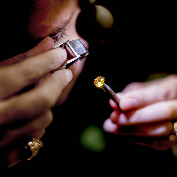 Une personne examine une petite pierre précieuse jaune à l'aide d'une loupe de bijoutier.