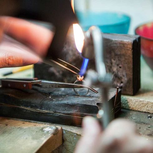 Un bijoutier soude une bague au chalumeau ; gros plan sur les mains, la flamme et les outils.