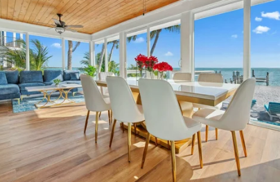 Sunroom with dining table and blue sectional, overlooking ocean.