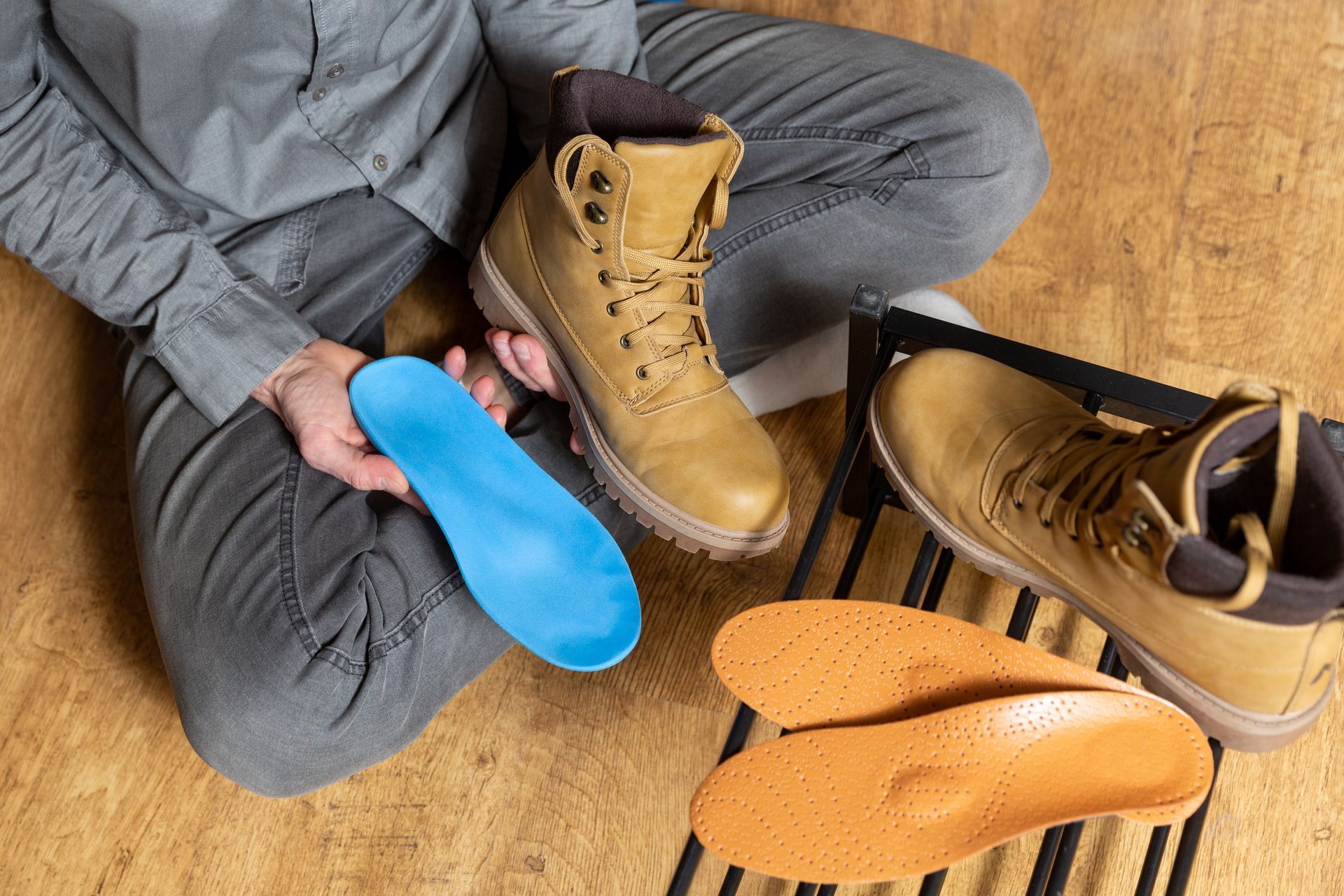 Une personne assise en tailleur tenant une chaussure dans une main et une semelle orthopédique dans l'autre.