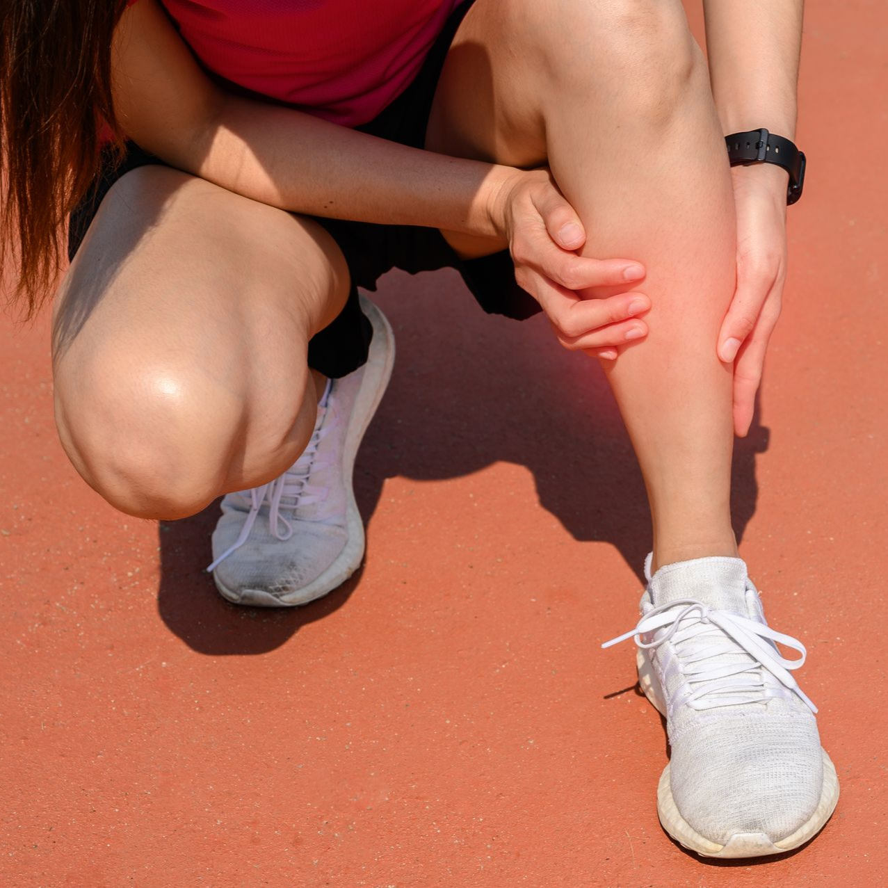 Un coureur accroupi sur une piste, se tenant la jambe.