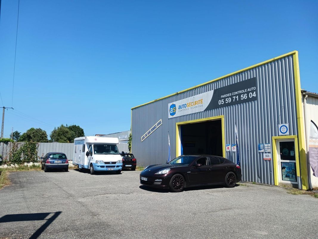 Extérieur d'un atelier automobile industriel avec un camion blanc, une voiture noire et un ciel bleu.
