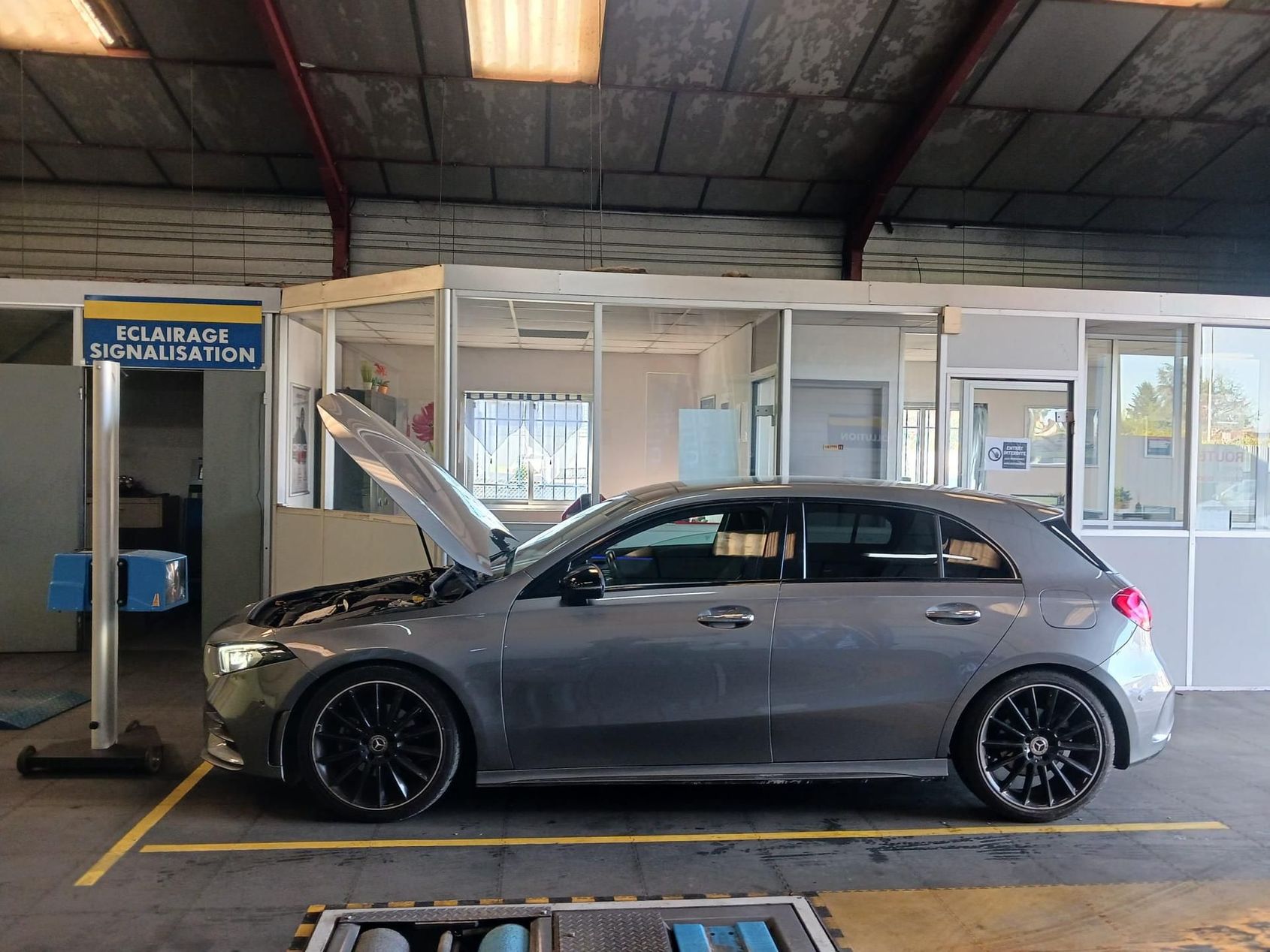 Berline grise à hayon, capot ouvert, dans un garage.