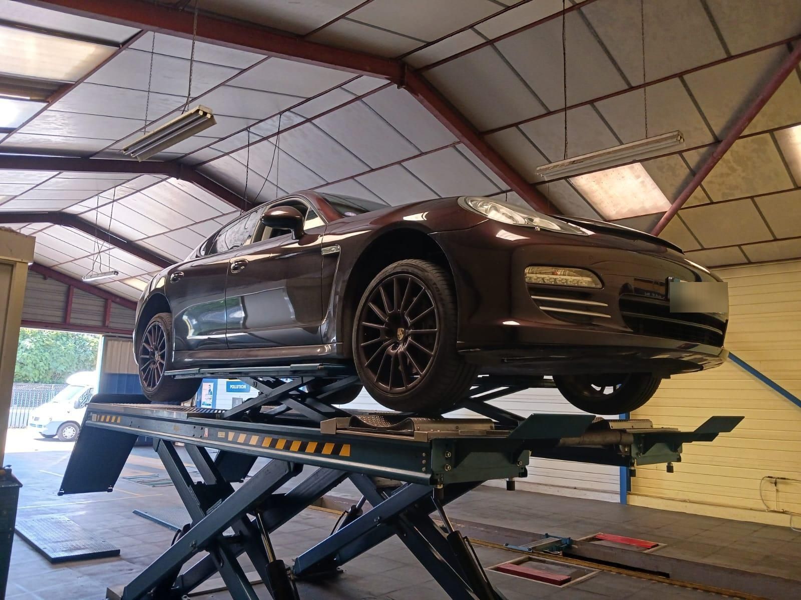 Voiture de sport gris foncé soulevée sur un pont élévateur à ciseaux à l'intérieur d'un garage ou d'un atelier.