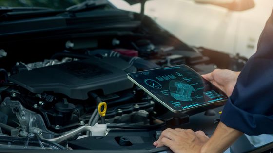 Un mécanicien utilise une tablette pour diagnostiquer un moteur de voiture dans un garage.