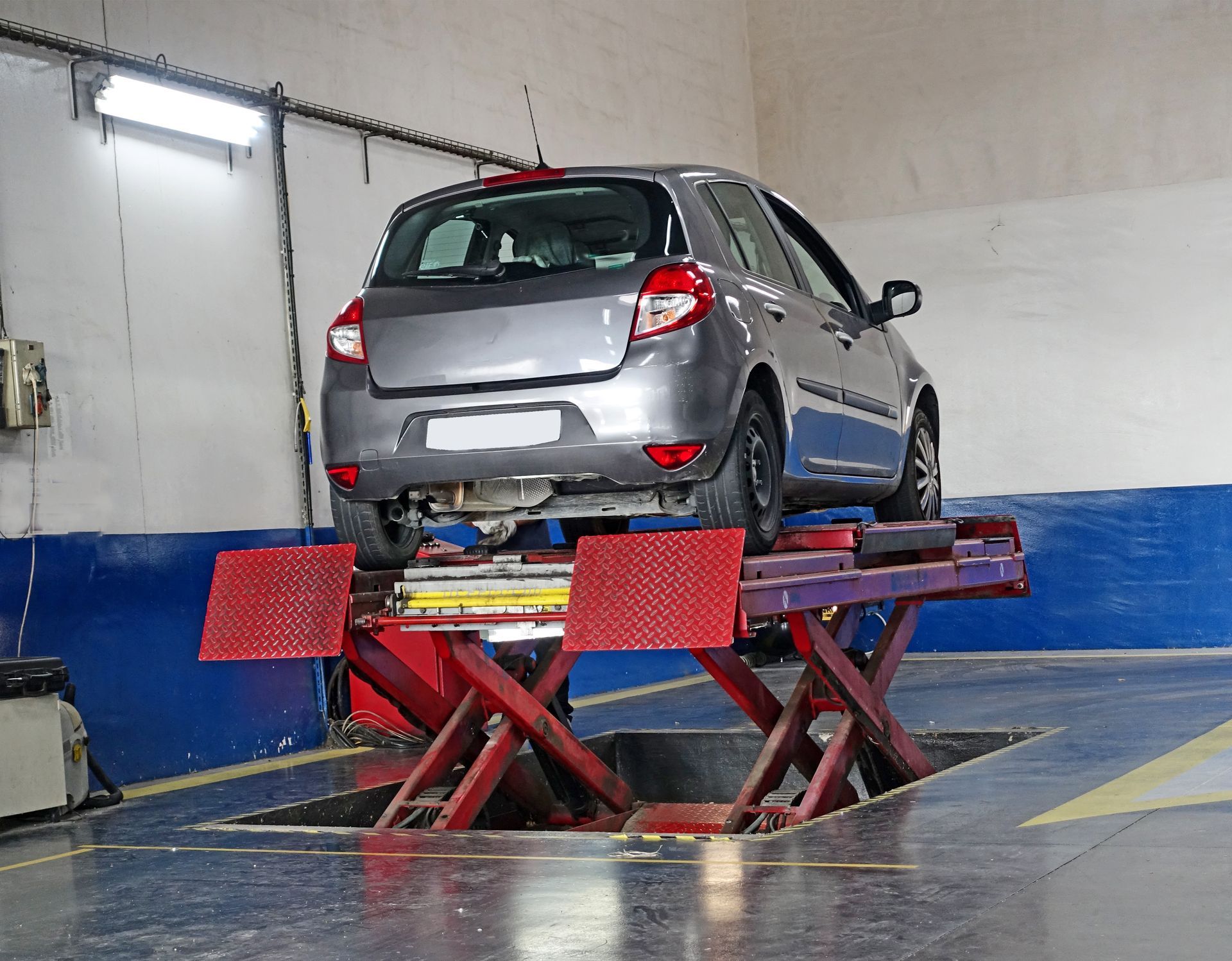 Voiture argentée sur un pont élévateur hydraulique rouge dans un garage de réparation automobile.