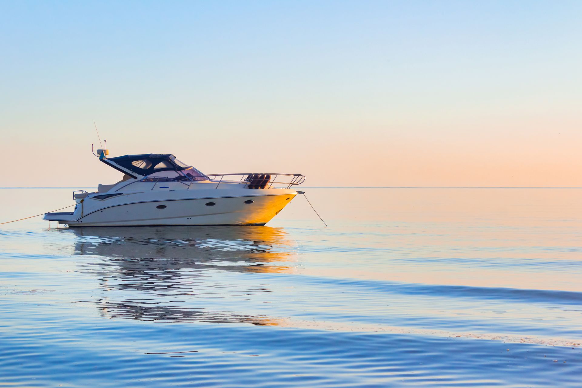 Yacht de luxe glissant sur une eau calme au coucher du soleil, avec un ciel aux teintes pastel et ses reflets.
