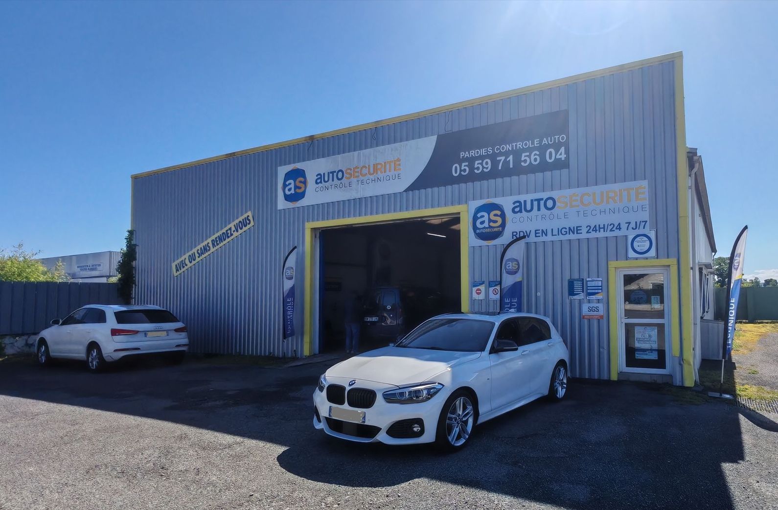 Façade d'un garage automobile avec deux voitures blanches garées devant par une journée ensoleillée.