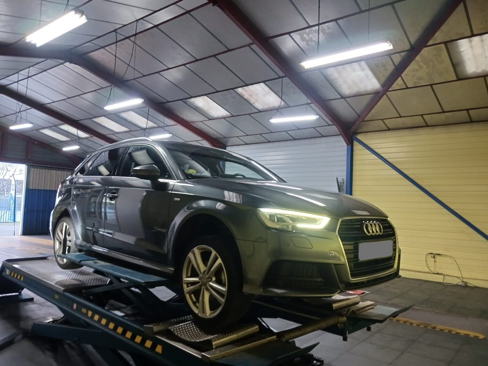 Un SUV Audi vert foncé sur un pont élévateur à l'intérieur d'un garage atelier.