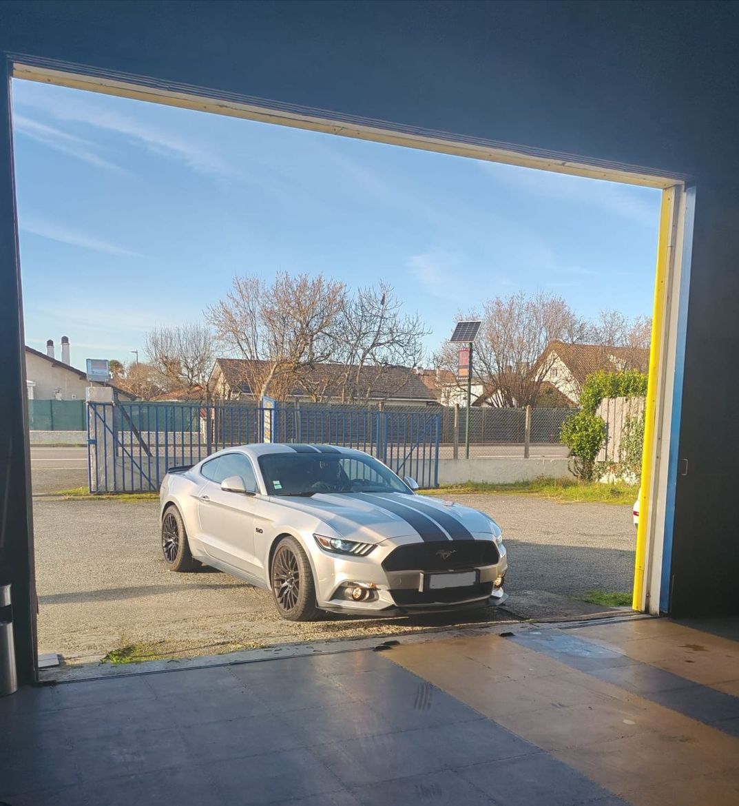 Voiture de sport argentée avec des bandes noires, garée devant une porte de garage ouverte.