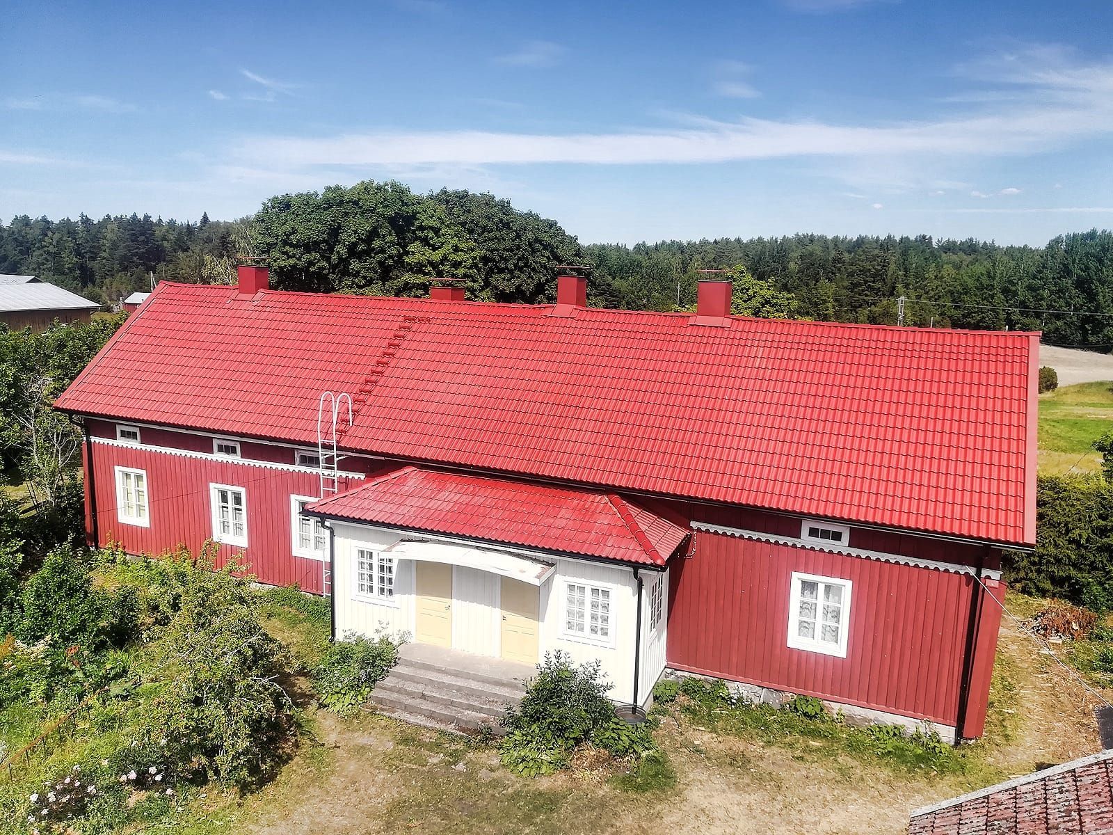 Punainen talo kirkkaanpunaisella katolla maaseudun maisemassa kirkkaan sinisen taivaan alla