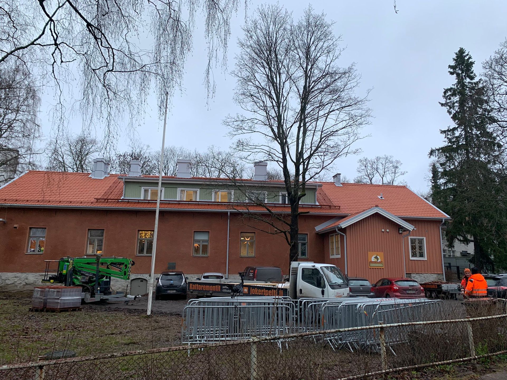 Tiilirakennus punaisella katolla ja rakennusajoneuvoja metalliesteiden takana pilvisenä päivänä