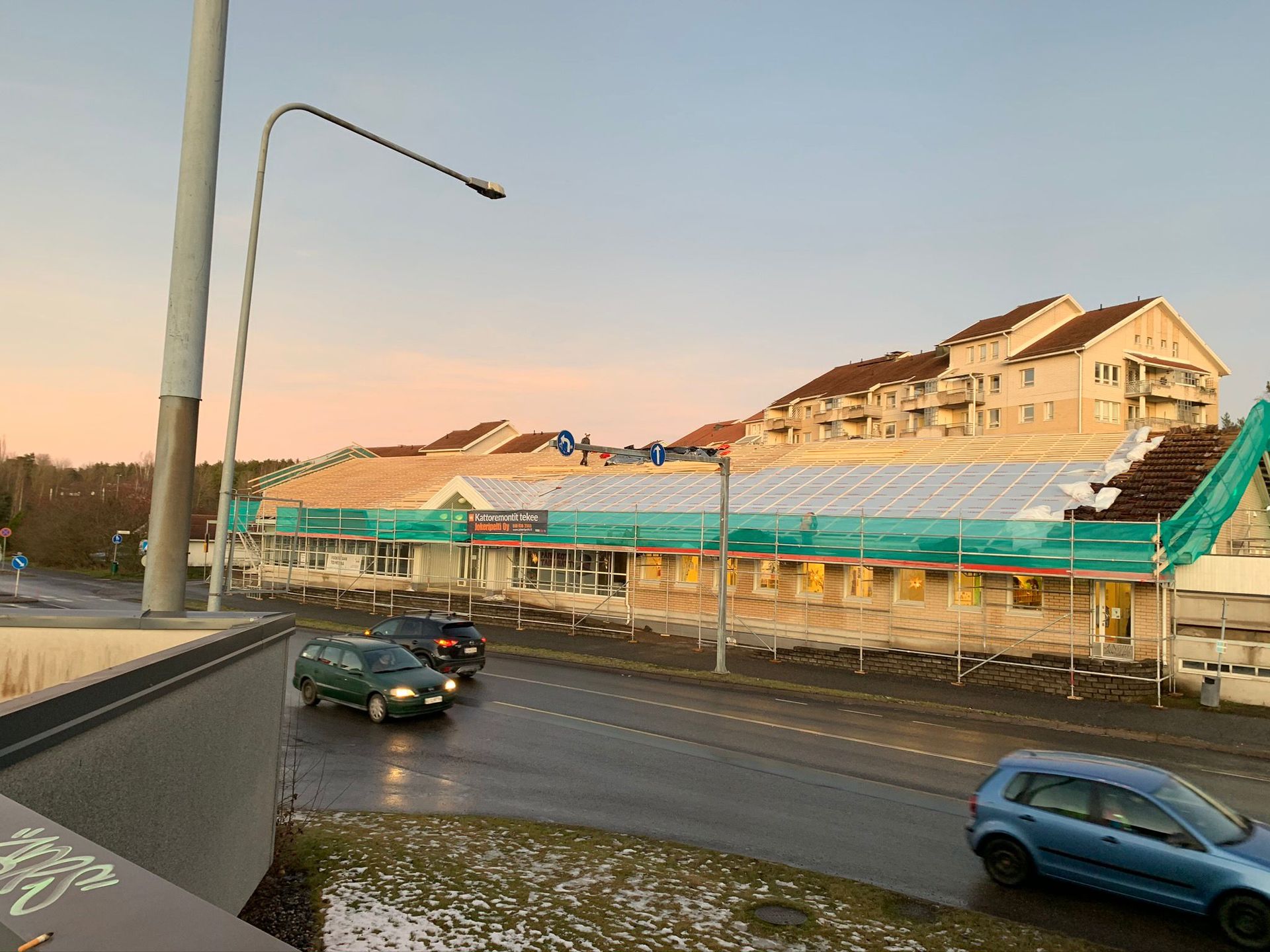 Aurinkoinen katu, jolla on autoja, raitiovaunupysäkki ja rinteellä tien varrella olevia rakennuksia