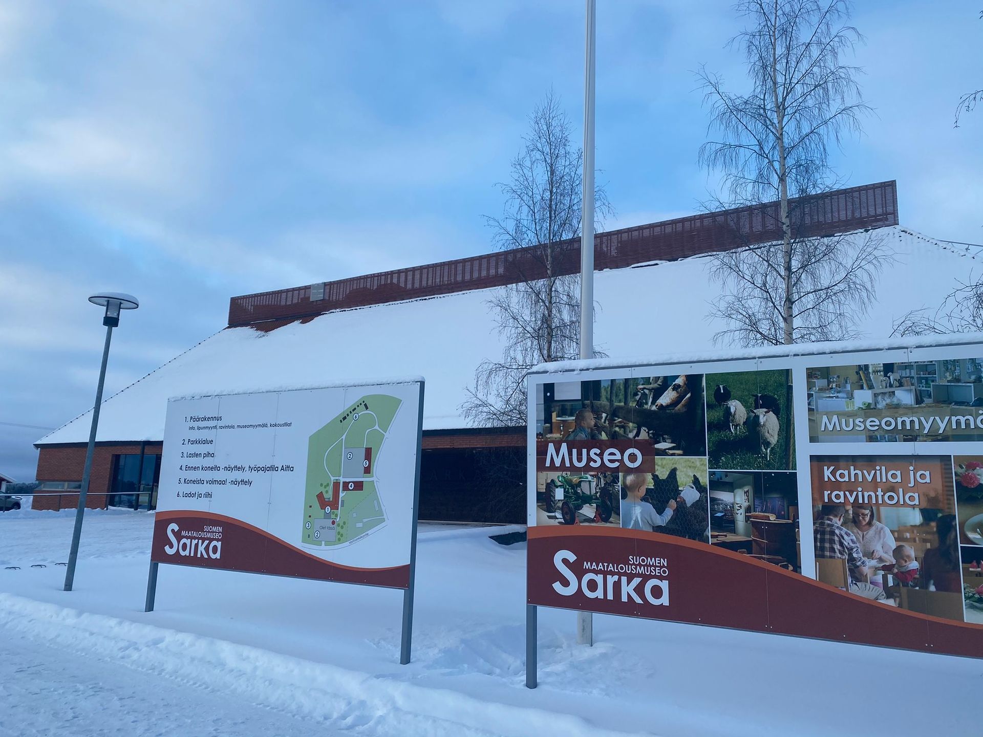 Lumiset museon sisäänkäynnin kyltit tien varrella pilvisen sinisen taivaan alla