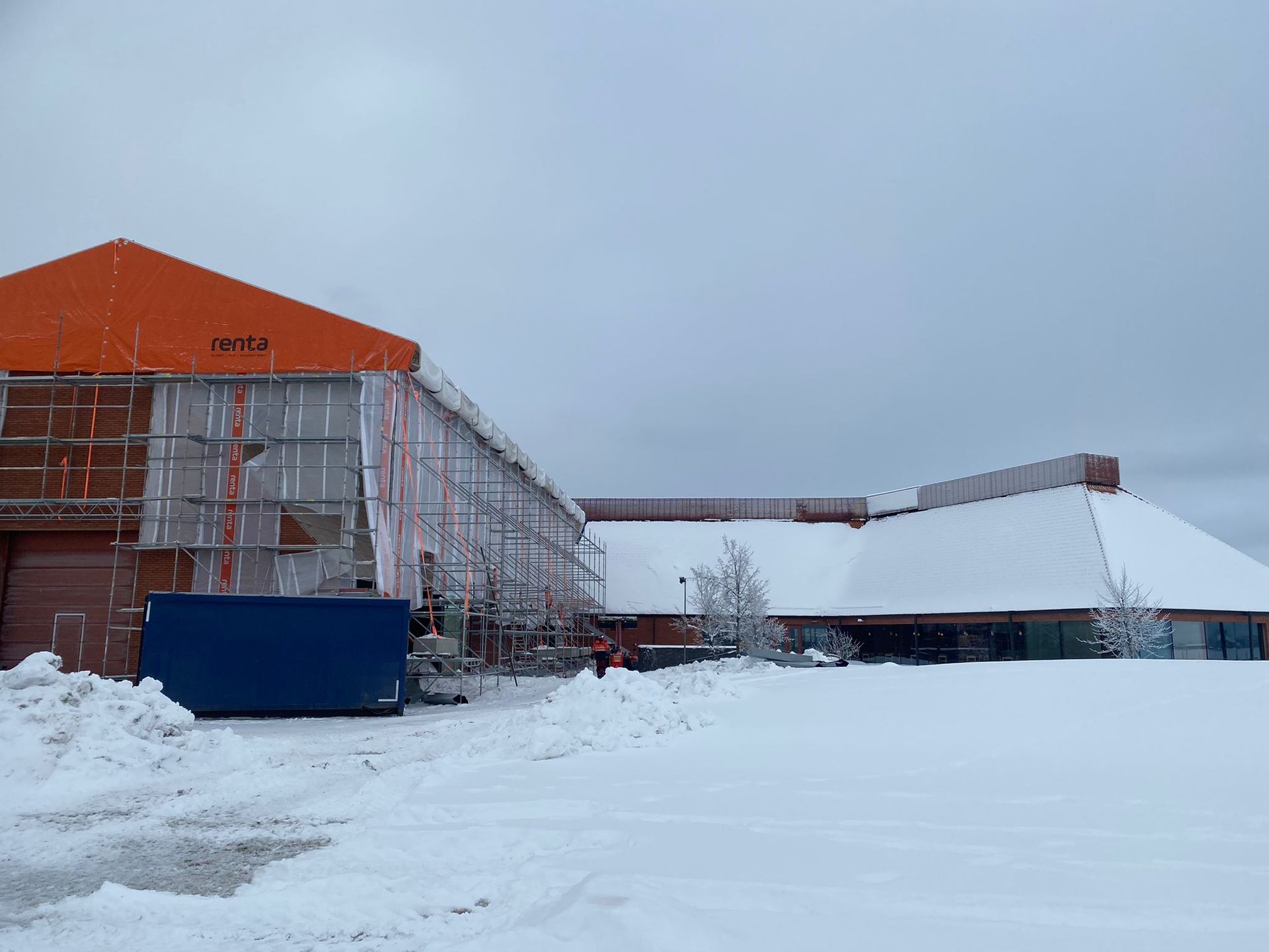 Rakenteilla olevia lumen peittämiä rakennuksia talvimaisemassa, oranssien kattojen ja rakennustelineiden kanssa.