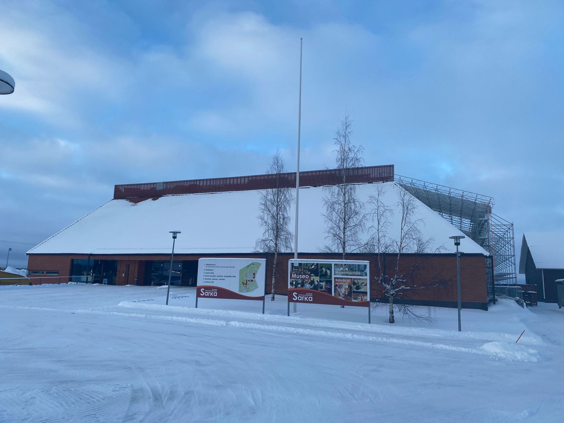 Lumen peittämä rakennus, jossa on korkea lipputanko ja tienvarsikyltit pilvisen taivaan alla