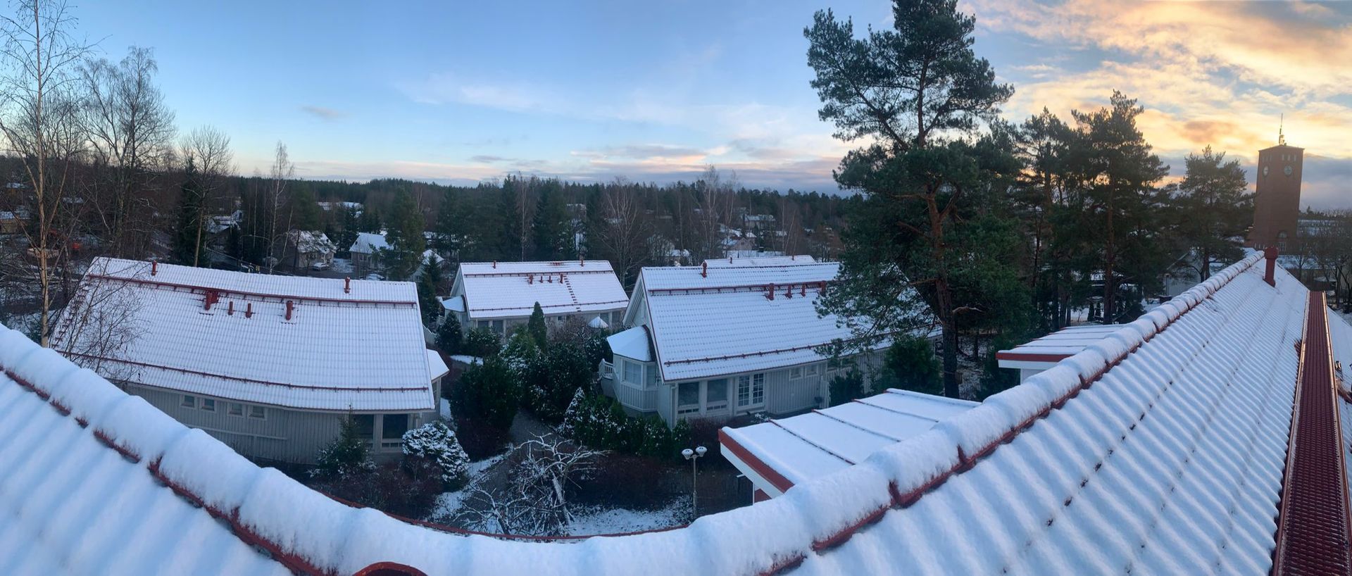 Lumisen lumen peittämiä kattoja ja puita auringonnousussa talvisen naapuruston yllä.