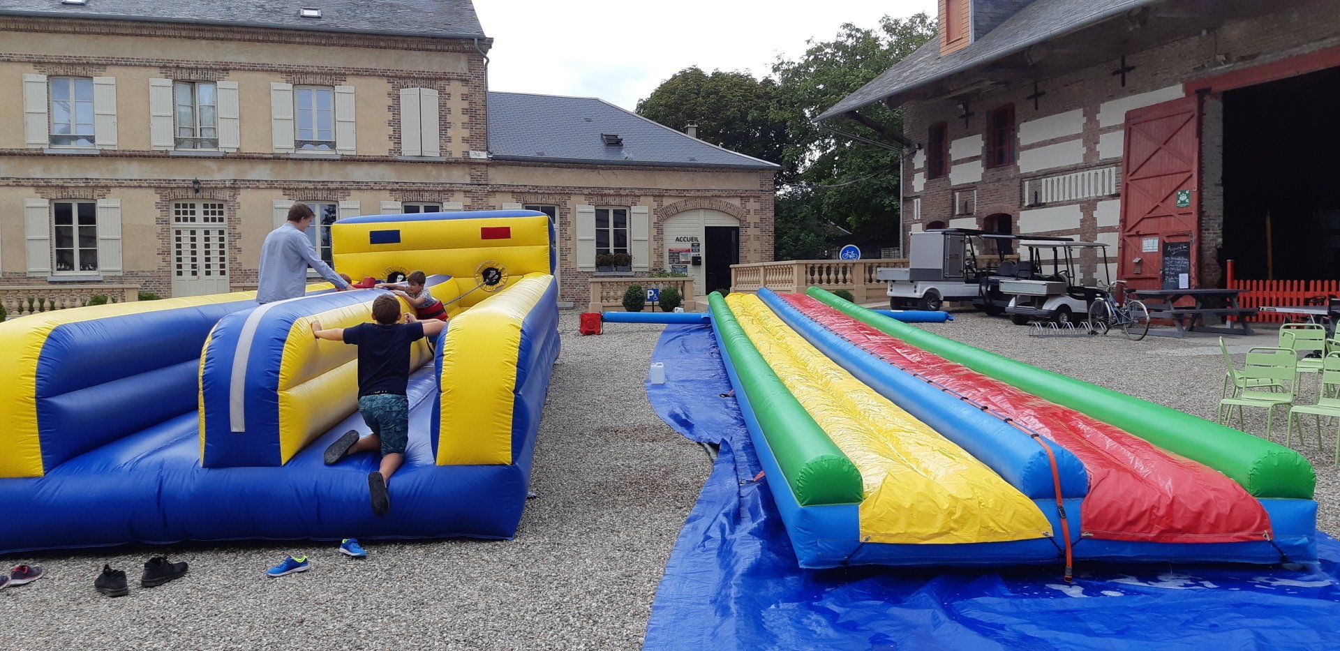 Des enfants jouent sur des toboggans gonflables en plein air. Des bâtiments se dressent en arrière-plan.