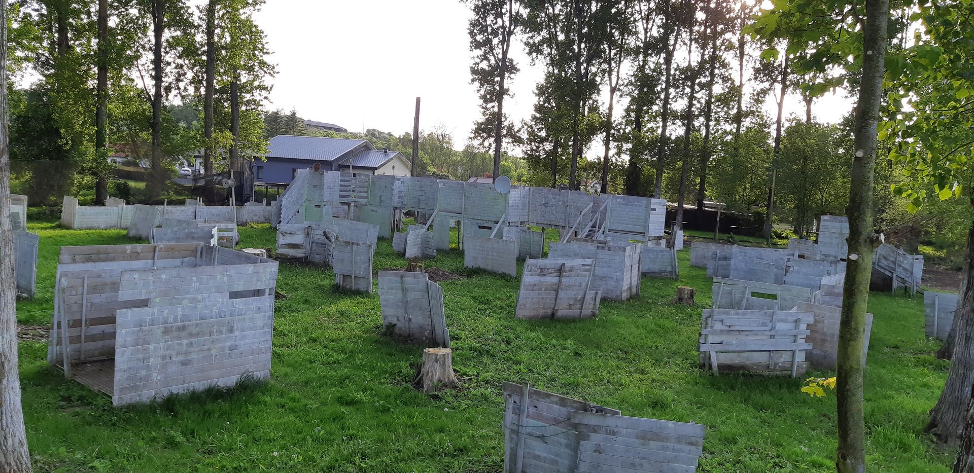Terrain de paintball avec bunkers en béton dans une zone herbeuse, entourée d'arbres.
