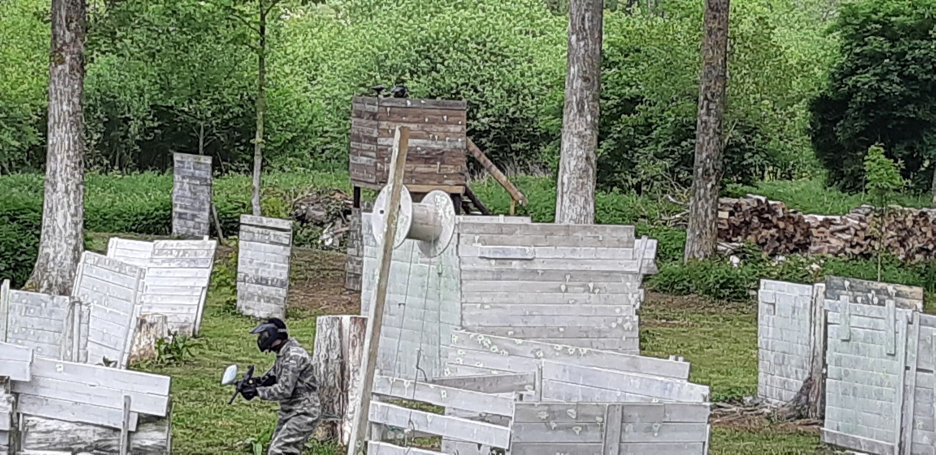 Une personne joue au paintball dans une zone boisée avec des bunkers.